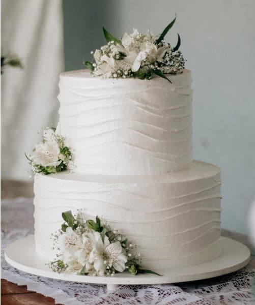 2 tiered white wedding cake with decorative flowers on each tier.