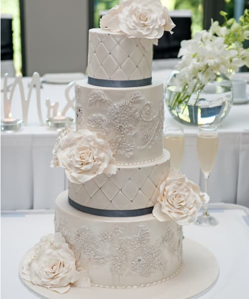 4 tiered wedding cake with blue ribbon tied around the tiers. While flowers made of fondue are placed on each tier.